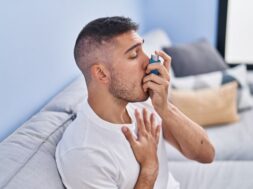 Young hispanic man using inhaler sitting on sofa at home