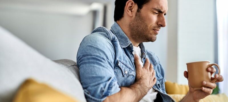Young man having a chest pain while drinking tea at home.