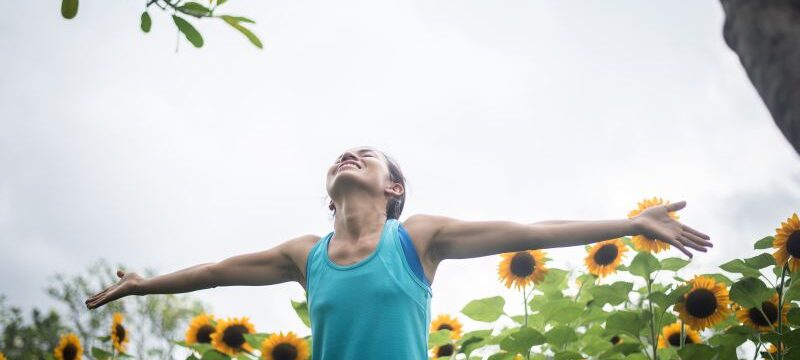 Beautiful woman with raising hands in a field of sunflowers in t