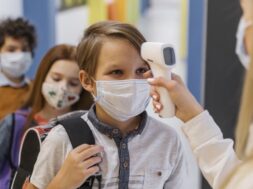 female-teacher-with-medical-mask-checking-student-s-temperature-school