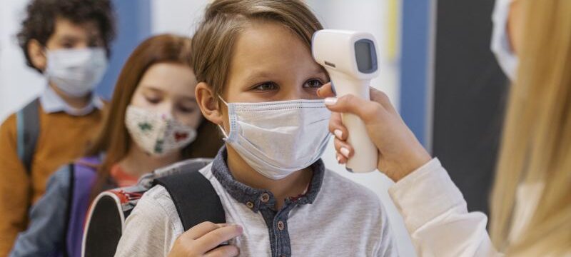 female-teacher-with-medical-mask-checking-student-s-temperature-school