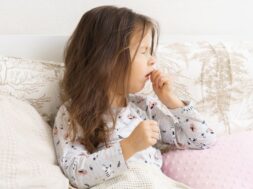 Poor, unfortunate little brunette preschooler child, girl in pajamas coughing, lying in soft bed. Sore throat, angina