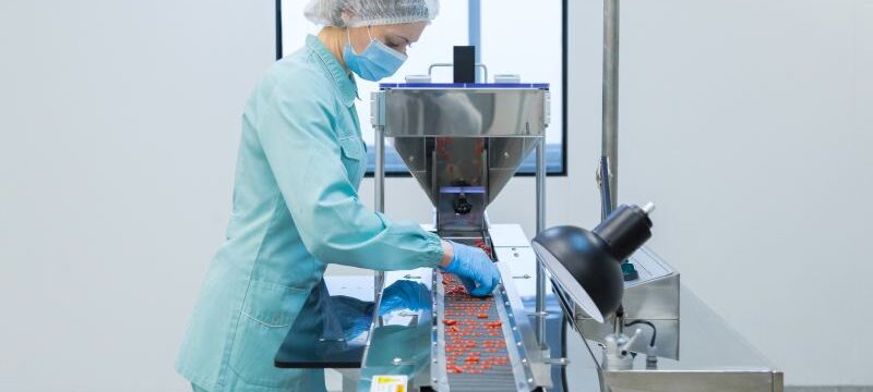 Pharmacy industry woman worker in protective clothing operating production of tablets in sterile working conditions
