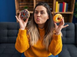 Young hispanic woman eating doughnuts at home looking at the camera blowing a kiss being lovely and sexy. love expression.