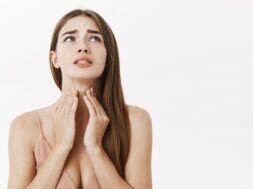 Woman getting ill before important meeting feeling discomfort and suffering from pain in throat touching neck frowning an clenching teeth from terrible feeling posing over gray background