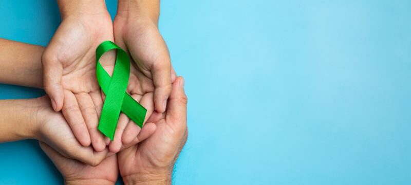 World Mental Health Day; green ribbon put in human’s hands on bl