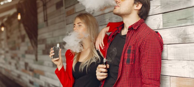Stylish young couple with vape in a city