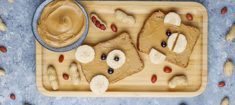 Funny bear and monkey face sandwich with peanut butter, banana and black currant,peanuts on grey concrete background,top view