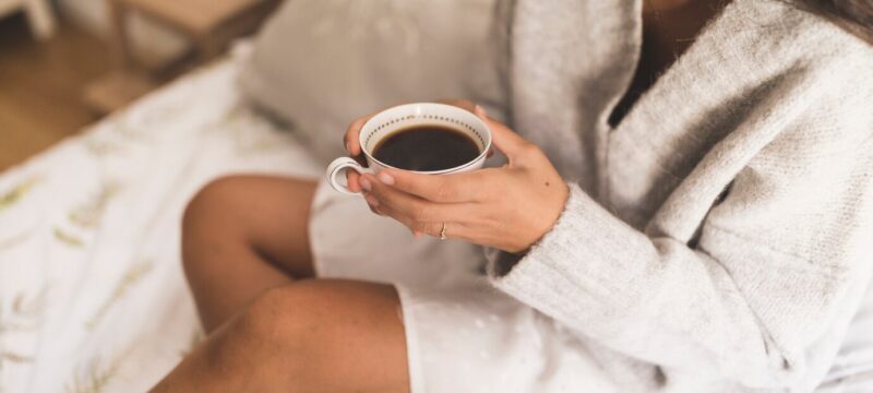 top-view-girl-sitting-bed-holding-coffee-cup_23-2147906551