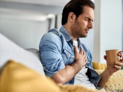 young-man-feeling-sick-holding-his-chest-pain-while-drinking-tea-living-room_637285-5913