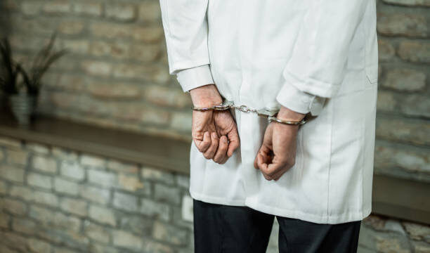 Hand close-up of unrecognizable doctor in handcuffs getting arrested.