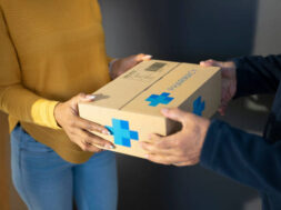 Woman receiving medicine box from delivery person.