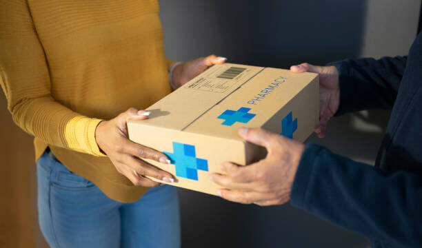 Woman receiving medicine box from delivery person.