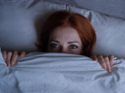 sleepless woman lying in bed with open eyes hiding under duvet at night