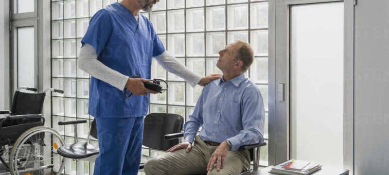 Male doctor talking to, comforting patient in clinic waiting room